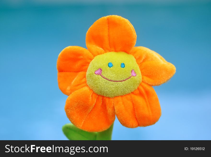 A happy, smiling bright orange and yellow toy flower with the turquoise blue water of a pool as the background. A happy, smiling bright orange and yellow toy flower with the turquoise blue water of a pool as the background