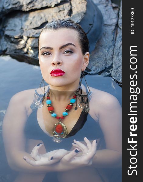 Glamorous brunette with bright makeup and accessories resting at a rock spa. Glamorous brunette with bright makeup and accessories resting at a rock spa