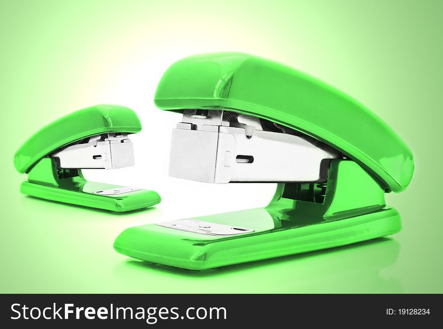 Close up of two  green office staplers isolated over pale green light effect. Close up of two  green office staplers isolated over pale green light effect