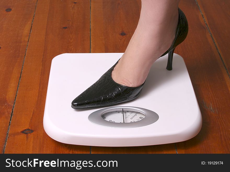 Stiletto foot on white bathroom scale on wood floor. Stiletto foot on white bathroom scale on wood floor