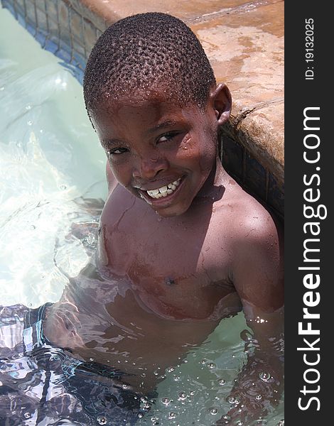 Young black african boy sitting on steps of swimming pool. Young black african boy sitting on steps of swimming pool