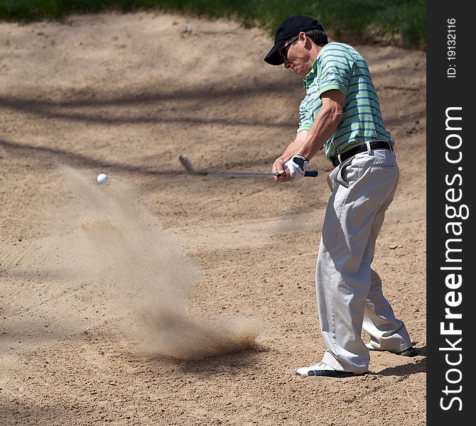 Golfer hits his golf ball out of the sand trap with the call frozen in the image after being hit.