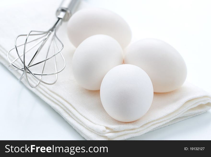 Metal whisk and fresh eggs, over white background.