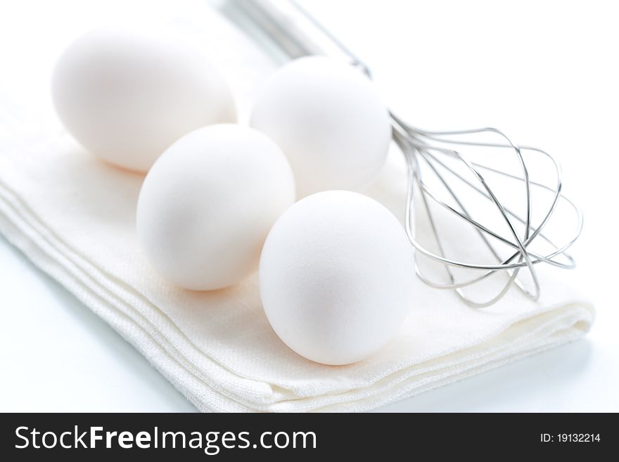 Metal whisk and fresh eggs, over white background.