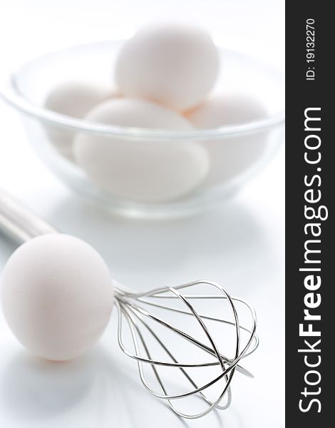 Metal whisk and fresh eggs in bowl, over white background.