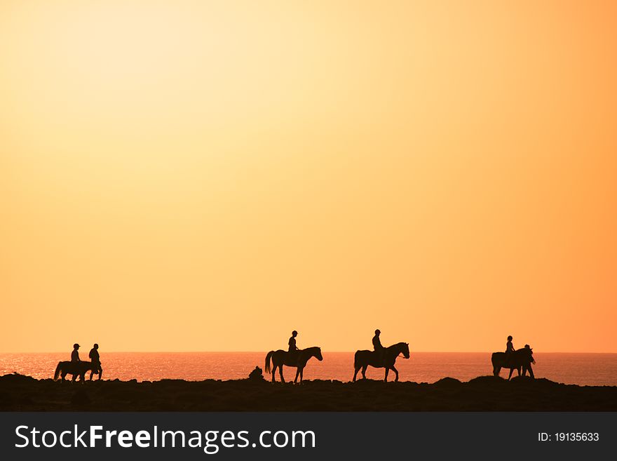 Silhouettes of the horse riders on the coast.