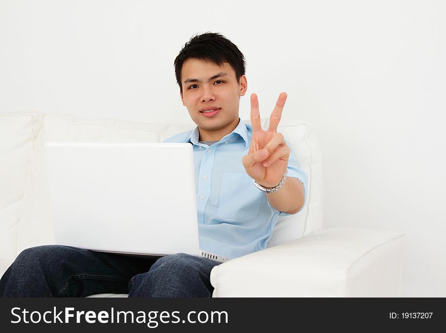 A man showing the victory sign while working with his laptop at home. A man showing the victory sign while working with his laptop at home