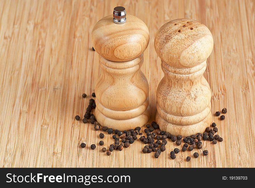 Salt and pepper grinders on a table, with pepper spread around