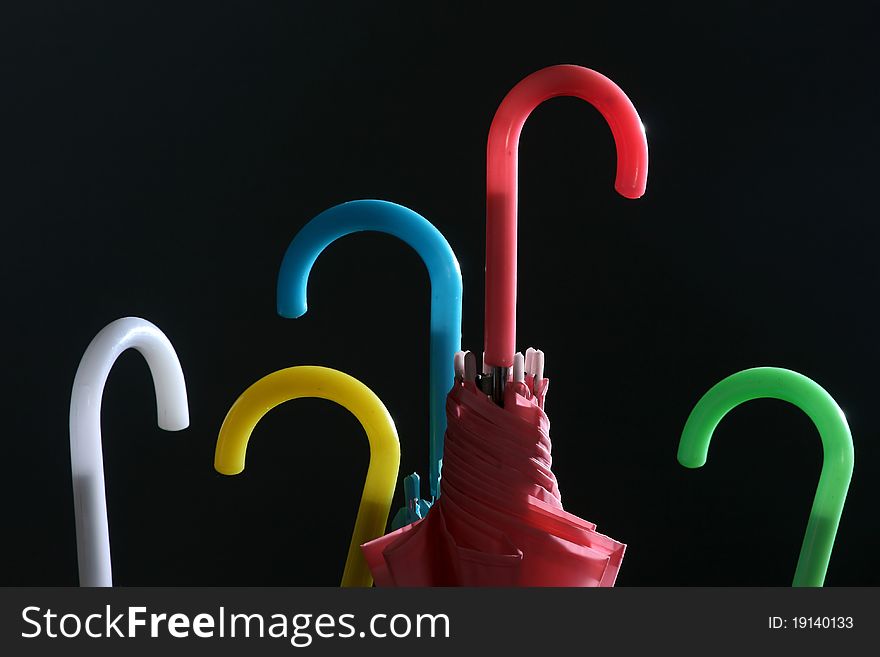 Very colourful nicely illuminated handles of the five umbrellas against the black background.