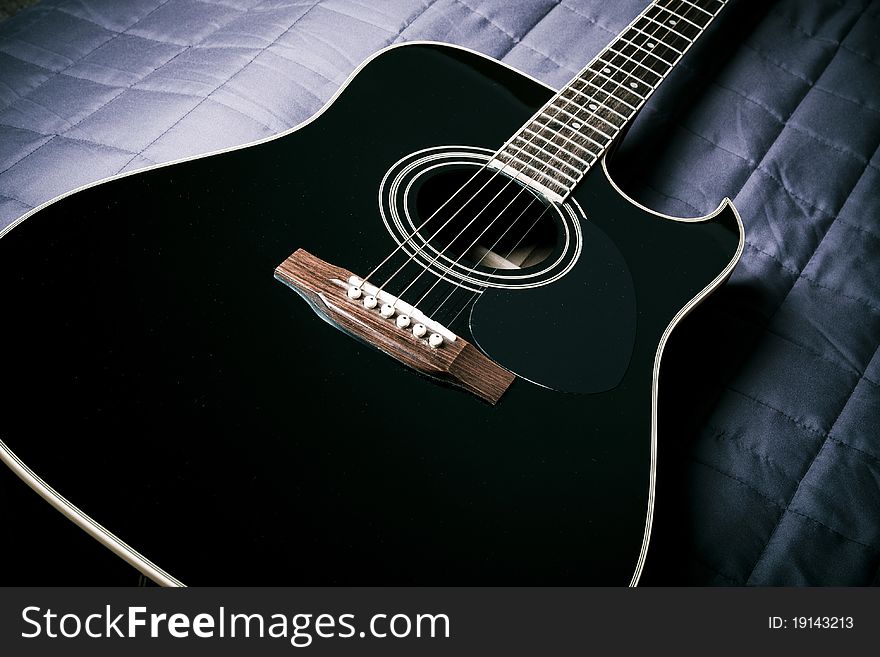 Black shiny acoustic guitar on bed. Black shiny acoustic guitar on bed