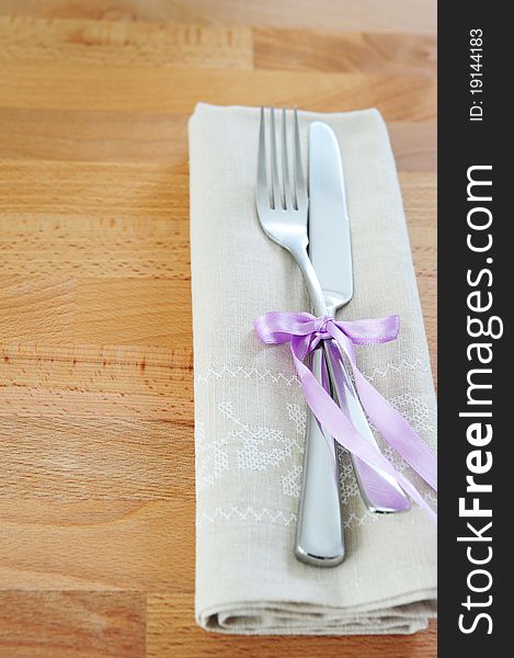Fork and knife, tied with purple ribbon, with a linen cloth on a wooden table. Fork and knife, tied with purple ribbon, with a linen cloth on a wooden table
