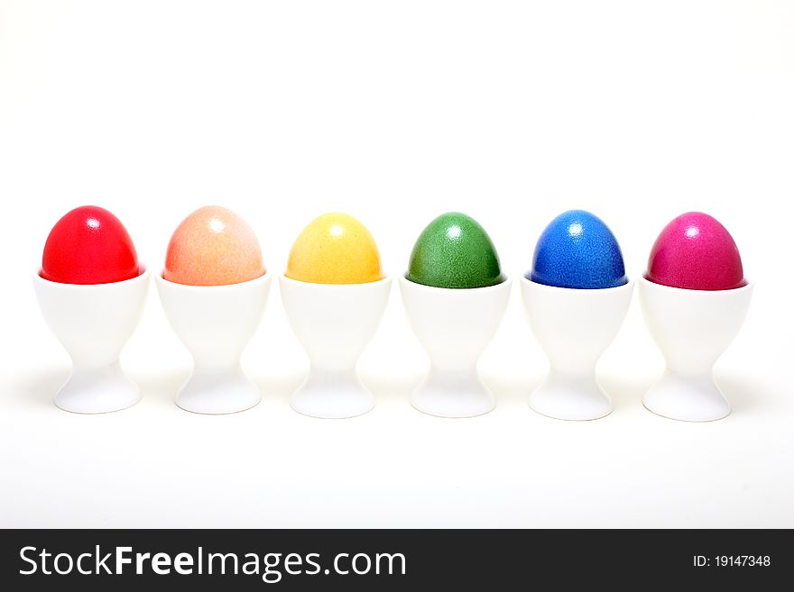 Six easter eggs in eggcups in a line on a white background