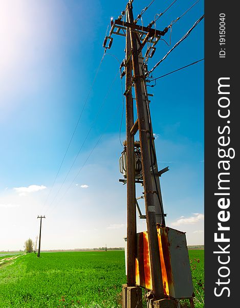 Power line against blue sky on green field