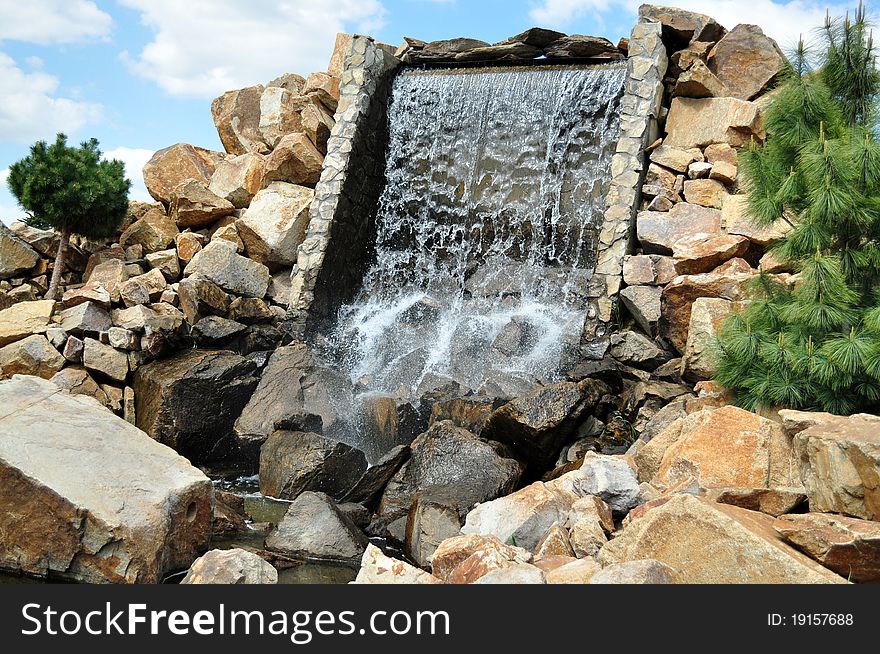 Beautiful artificial waterfall in a particular garden with rocks and trees