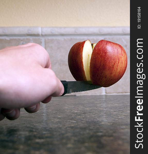 Red apple being cut in half with a sharp knife being held up by one single toothpick