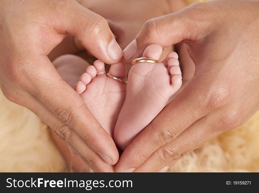 A father holding his baby's feet with fingers showing a heart shape, the baby's toes has it's parents wedding bands on. A father holding his baby's feet with fingers showing a heart shape, the baby's toes has it's parents wedding bands on.