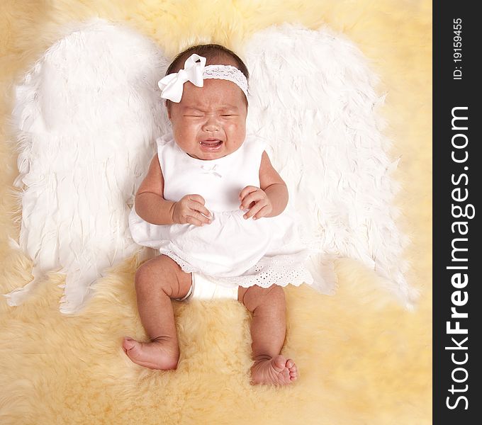 A beautiful oriental baby laying on a fur rug with her white angel wings on her back, with a sad expression on her face. A beautiful oriental baby laying on a fur rug with her white angel wings on her back, with a sad expression on her face.
