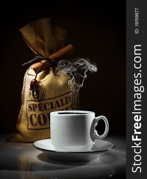Composition of white cup and sack of coffee beans on dark black background