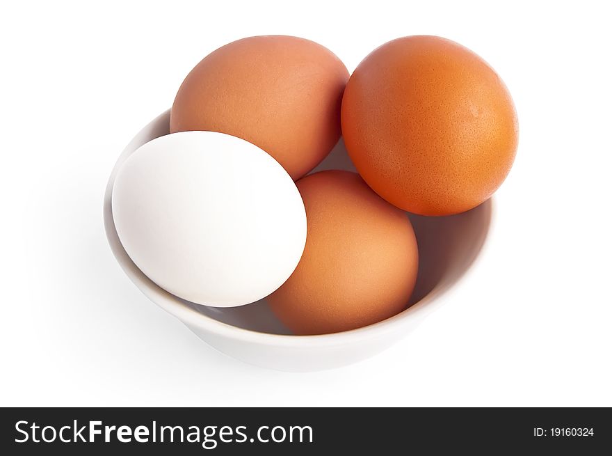 The three brown and one white egg in a bowl with a light shadow on a white background. The three brown and one white egg in a bowl with a light shadow on a white background