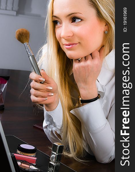 A blond girl with make-up scattered upon the laptop in the office. A blond girl with make-up scattered upon the laptop in the office