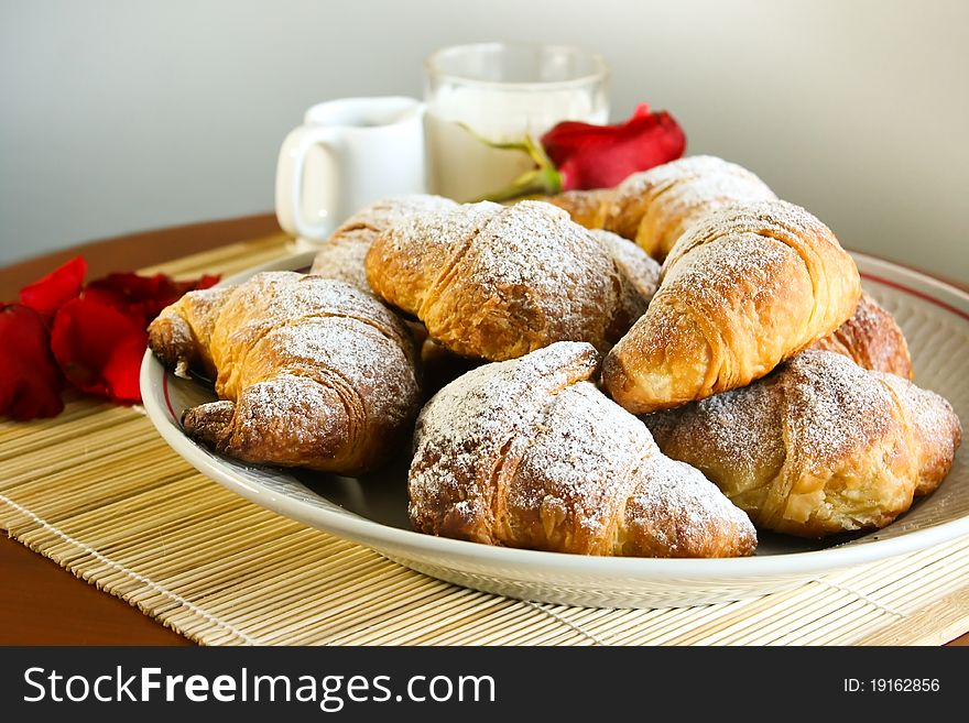 Table with a plate of croissants and a pink and red petals. Table with a plate of croissants and a pink and red petals.