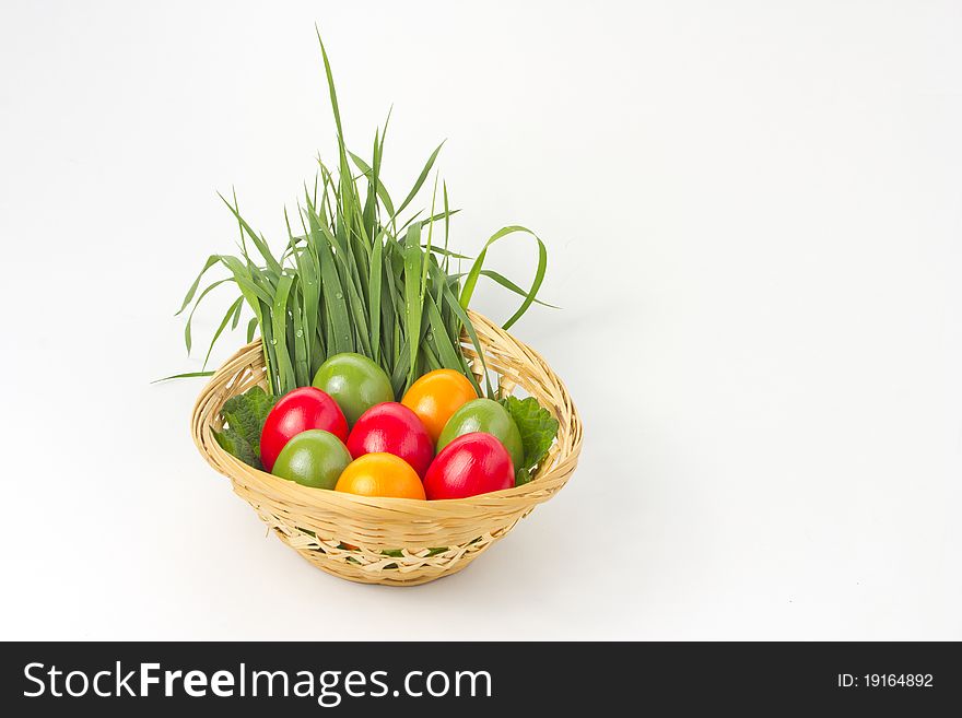 Colored eggs on grass and leaf in basket on white background. Colored eggs on grass and leaf in basket on white background.