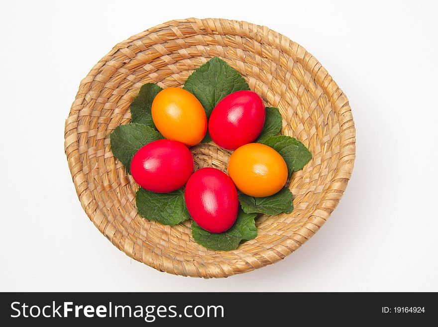 Red and yellow eggs laying on leafs in a basket on white background. Red and yellow eggs laying on leafs in a basket on white background.