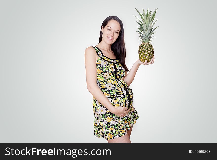 Pregnant woman holding pinapple in her hand studio shoot isolated on grey