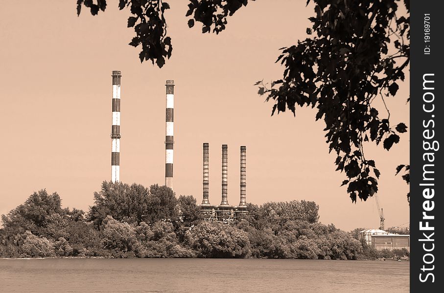 Factory by Danube river, several chimneys behind trees in sepia tones. Factory by Danube river, several chimneys behind trees in sepia tones