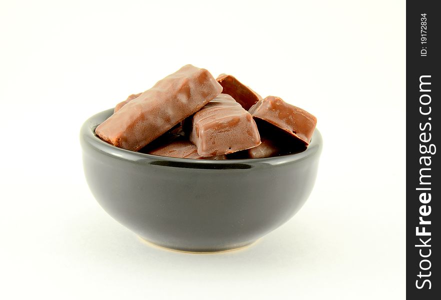 Pieces of chocolate candy in a black ceramic bowl on a white background. Pieces of chocolate candy in a black ceramic bowl on a white background