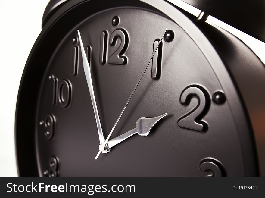 Close up of black alarm clock with focus on hour hand, on white background. Close up of black alarm clock with focus on hour hand, on white background.