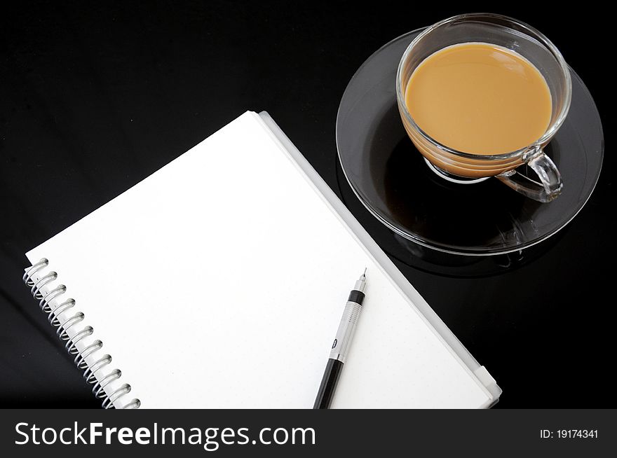 Clear cup of coffee with notebook on dark background