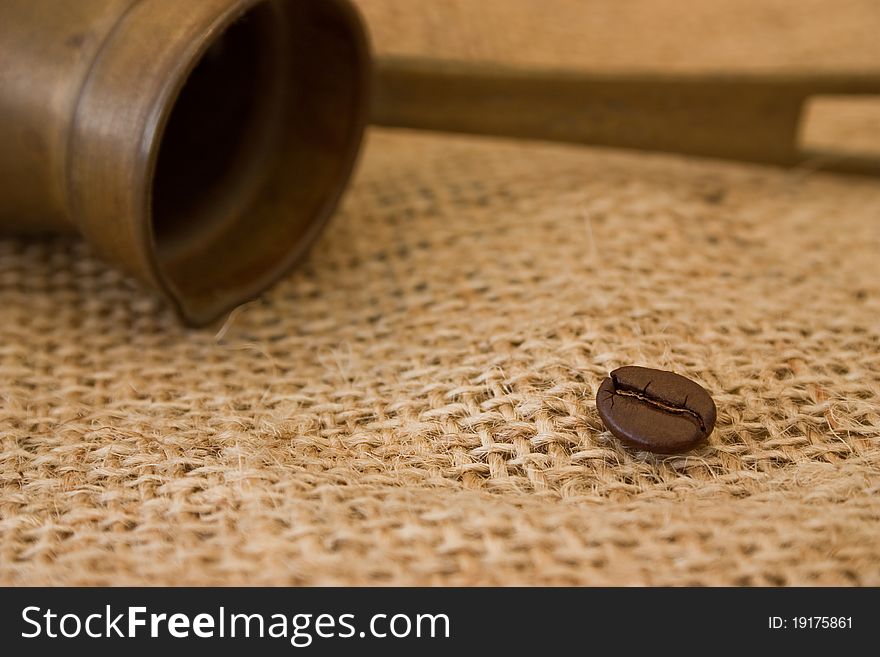 Single coffee bean with coffee pot on burlap sack background. Single coffee bean with coffee pot on burlap sack background