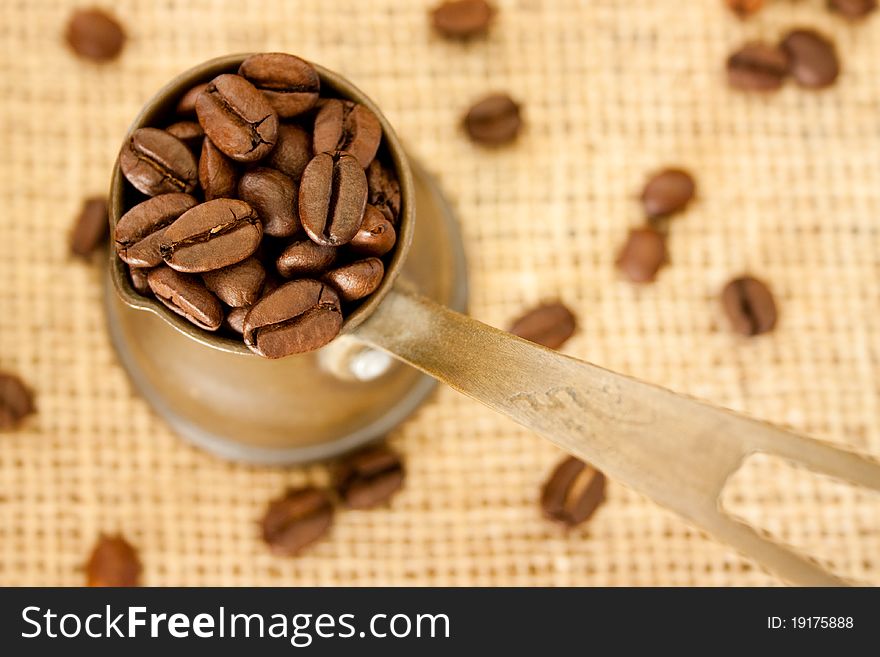 Coffee beans in a coffee pot on burlap sack background