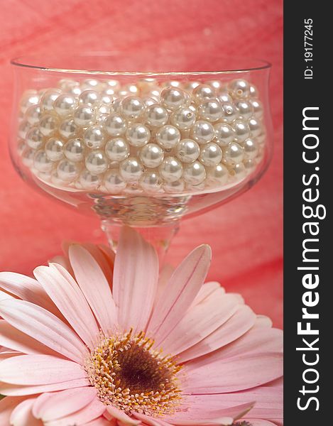 Pearls in a crystal glass, flower on pink background. Pearls in a crystal glass, flower on pink background