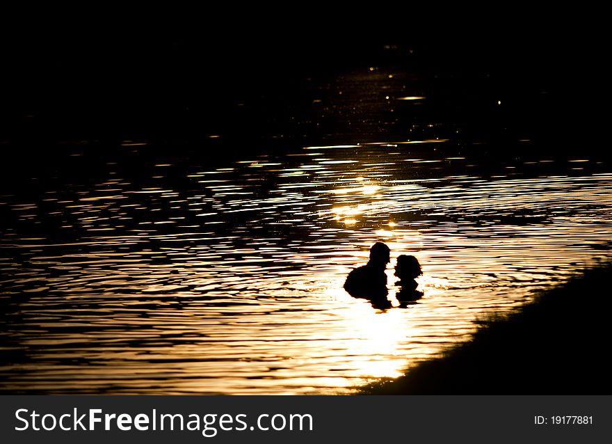 A man and a woman in love in the lake in rays of sun on sunset. A man and a woman in love in the lake in rays of sun on sunset