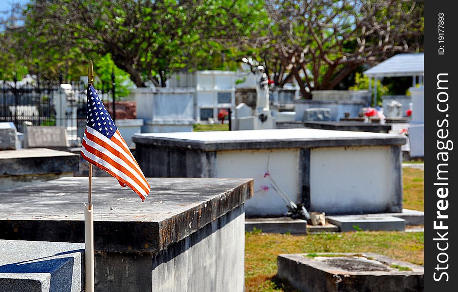 A Small American Flag Waves Over An Old Cemetery With Selective Focus On Flag. A Small American Flag Waves Over An Old Cemetery With Selective Focus On Flag