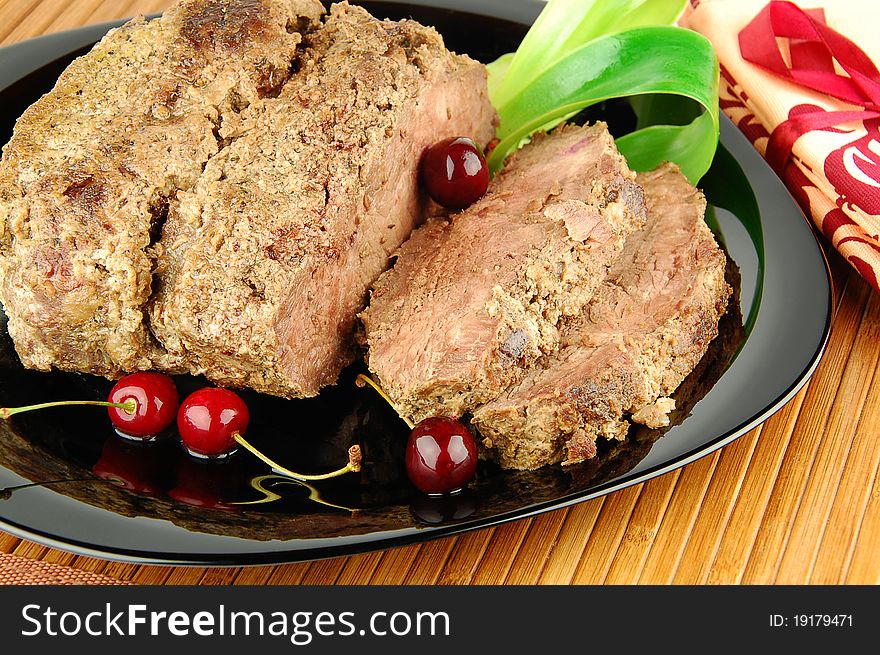 Succulent roast beef meat slices with cherry on a black plate. Succulent roast beef meat slices with cherry on a black plate
