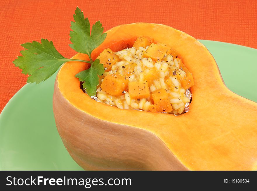 Half pumpkin filled with pumpkin risotto served on a green plate