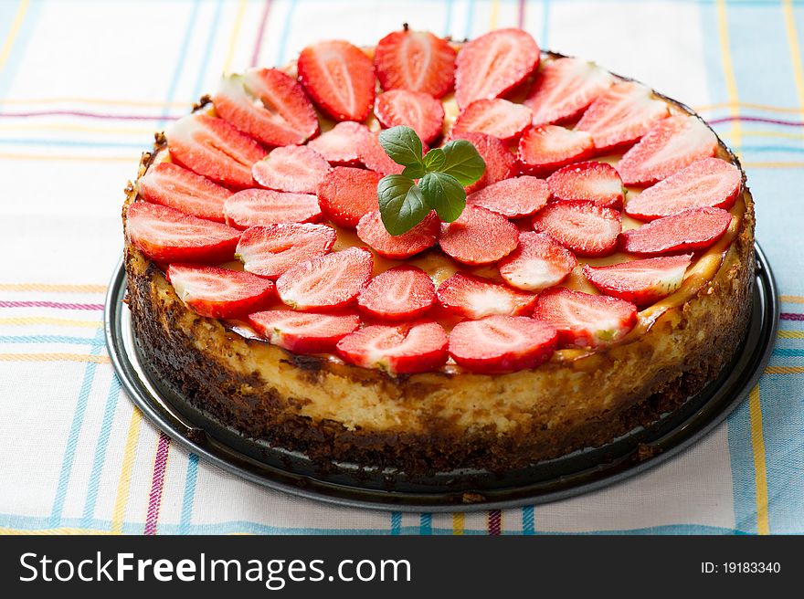 Photo of a whole good looking vanilla cheesecake topped with sliced strawberries and mint. Photo of a whole good looking vanilla cheesecake topped with sliced strawberries and mint.