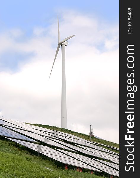 Solar panel and wind mill in front of a tree and blue sky. Solar panel and wind mill in front of a tree and blue sky