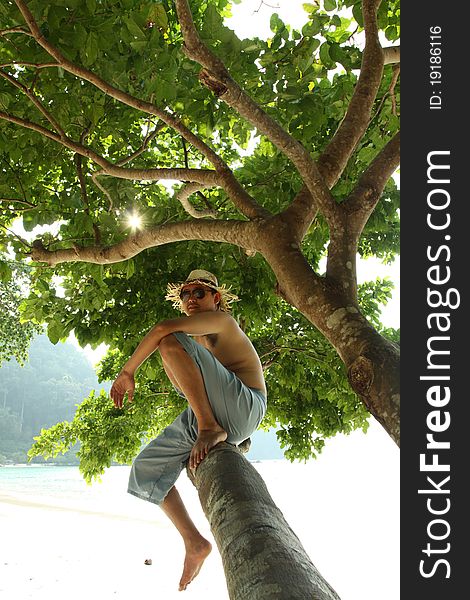 A man dressed islander sit on a big branch of tree by the sea. A man dressed islander sit on a big branch of tree by the sea.