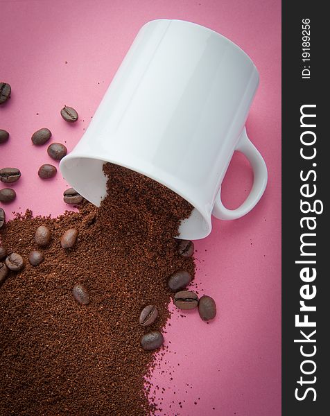 Cup with coffee grind and coffee beans spilled on a pink background. Cup with coffee grind and coffee beans spilled on a pink background