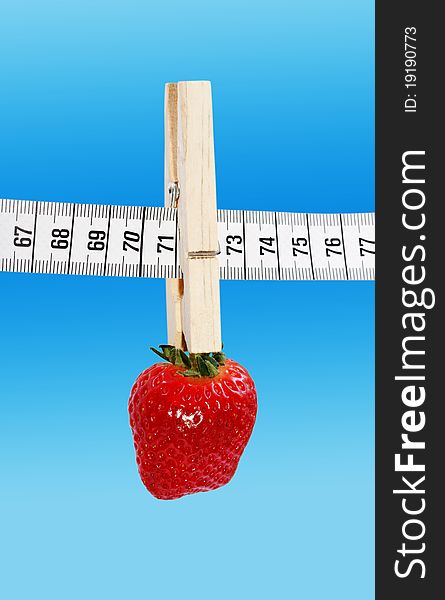 One strawberry hanging on the measuring tape with clothespin isolated on a blue surface. One strawberry hanging on the measuring tape with clothespin isolated on a blue surface.