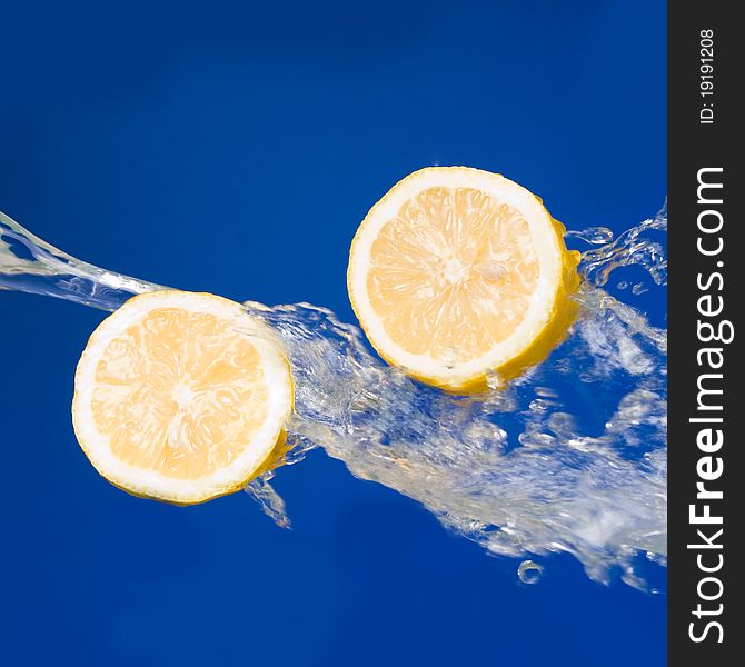 Two halves of lemon in the splashes of water on a blue background