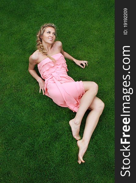 Young attractive blond girl in the pink dress on the green grass. Young attractive blond girl in the pink dress on the green grass