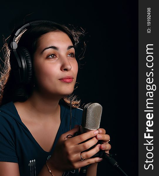 Singin' girl with a microphone and head-phones on the black background