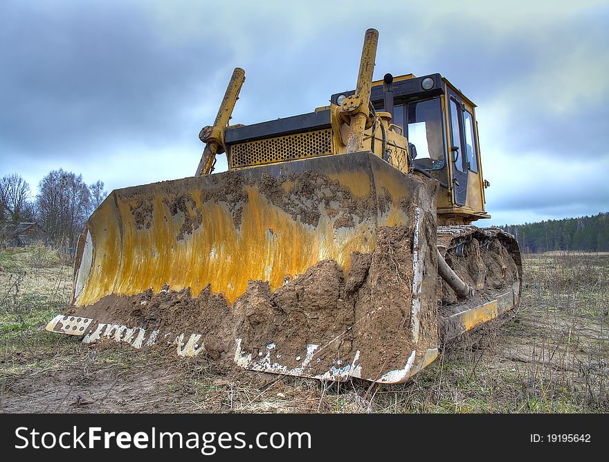 Yellow bulldozer, standing against a background of green forest and blue sky