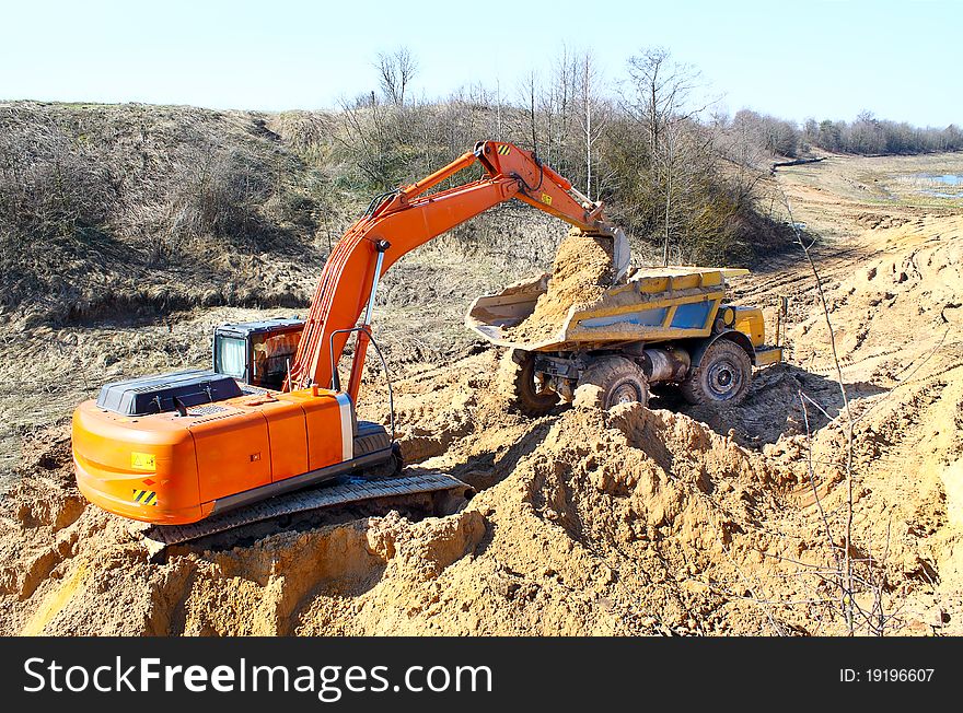 Excavator loading truck shot against the background of the pit and blue sky. Excavator loading truck shot against the background of the pit and blue sky