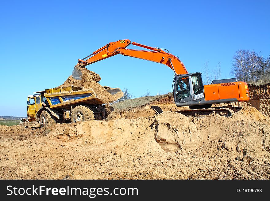 Excavator loading truck shot against the background of the pit and blue sky. Excavator loading truck shot against the background of the pit and blue sky